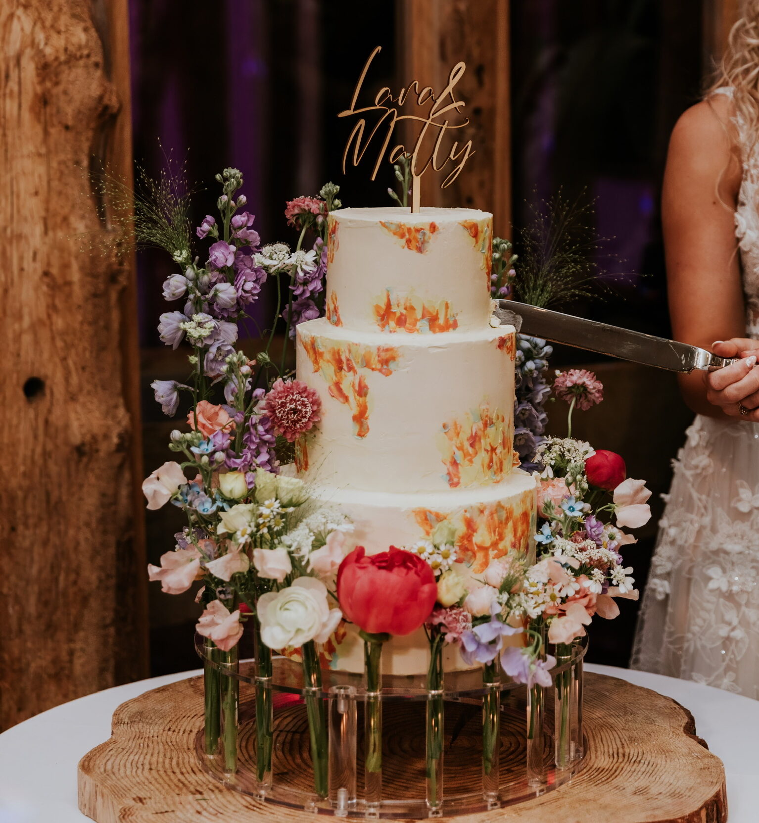 Swiss meringue buttercream encasing a three tier wedding cake to create a smooth, classic finish with flecks of bright pastel colour from orange, yellow and blue