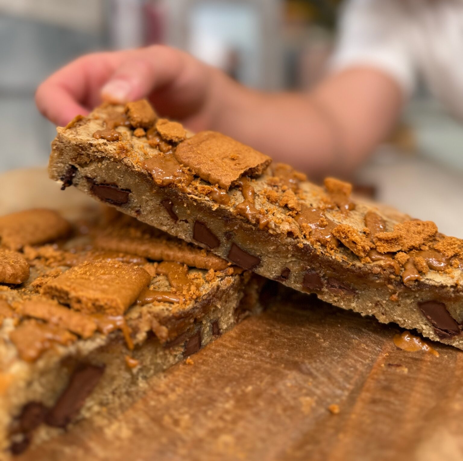 A slab of Biscoff blondie cut in half to show the gooey centre alongside the chunks of chocolate, topped with Biscoff biscuits and spread