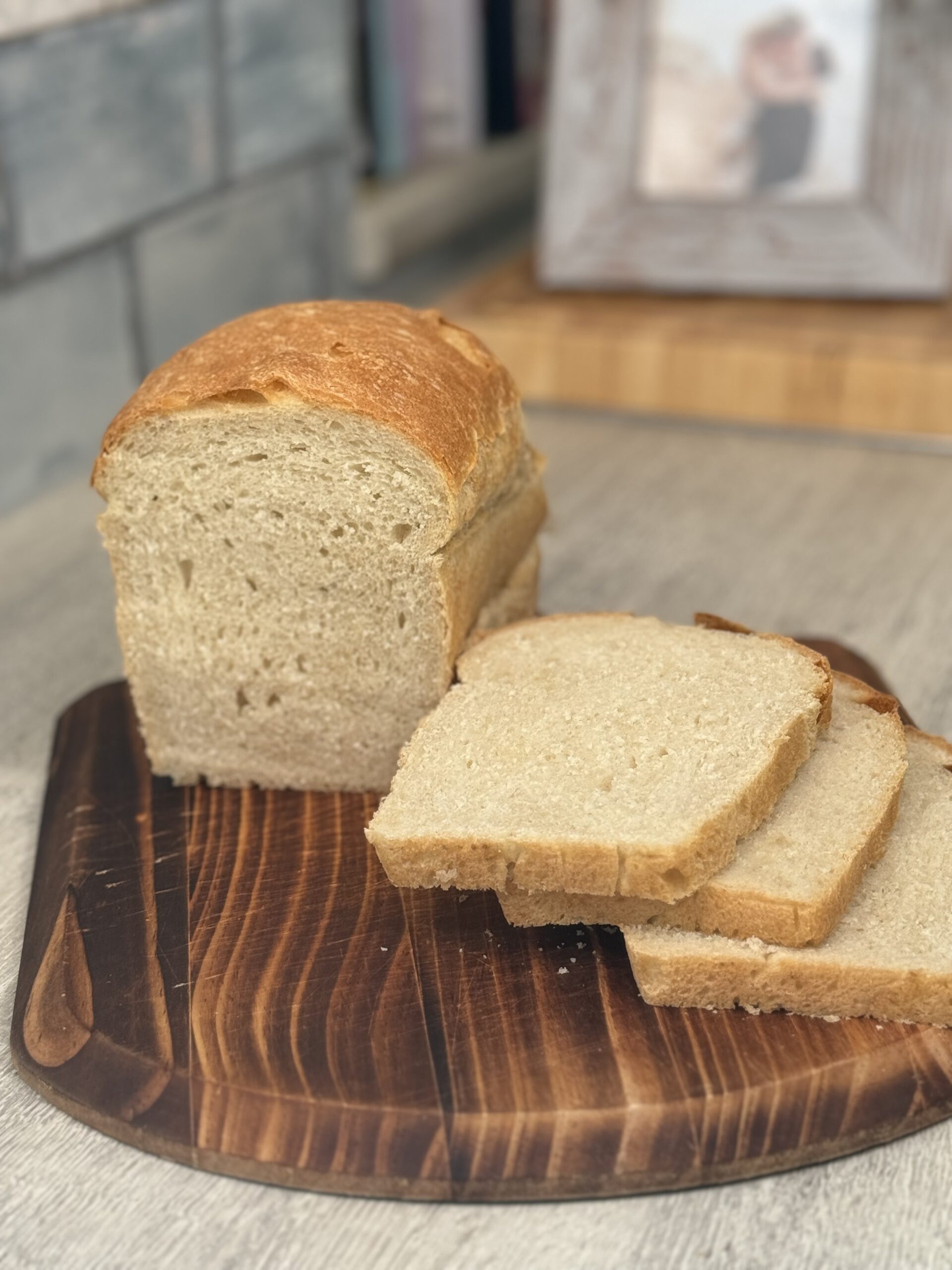 A crusty white loaf of bread that has been sliced to show the inside on a wooden chopping board.