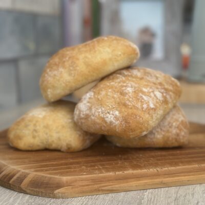 Ciabatta rolls placed onto a wooden chopping board, stacked on top of each other