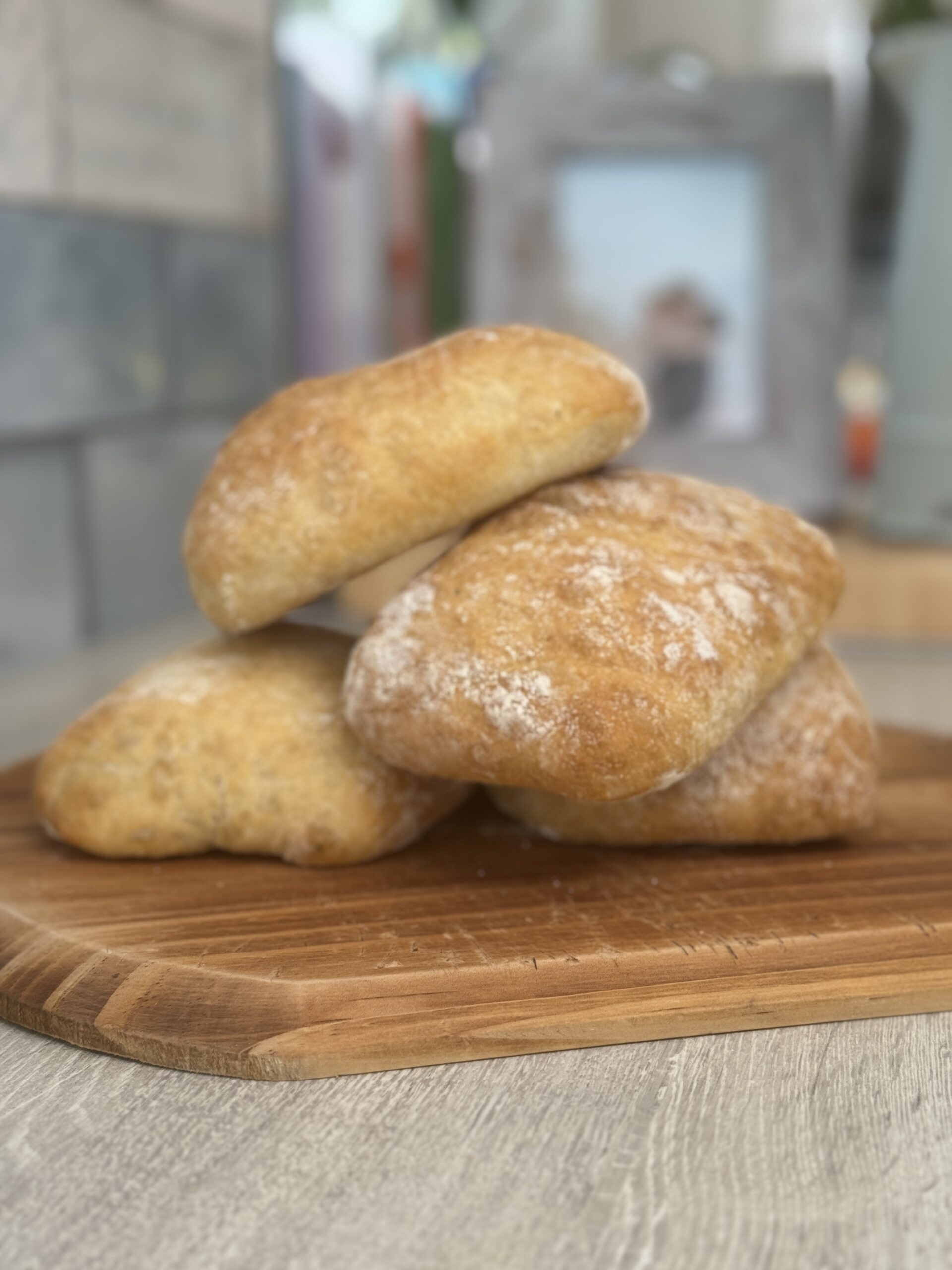 Ciabatta rolls placed onto a wooden chopping board, stacked on top of each other