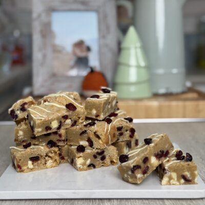 Slices of cranberry and white chocolate blondie stacked on board